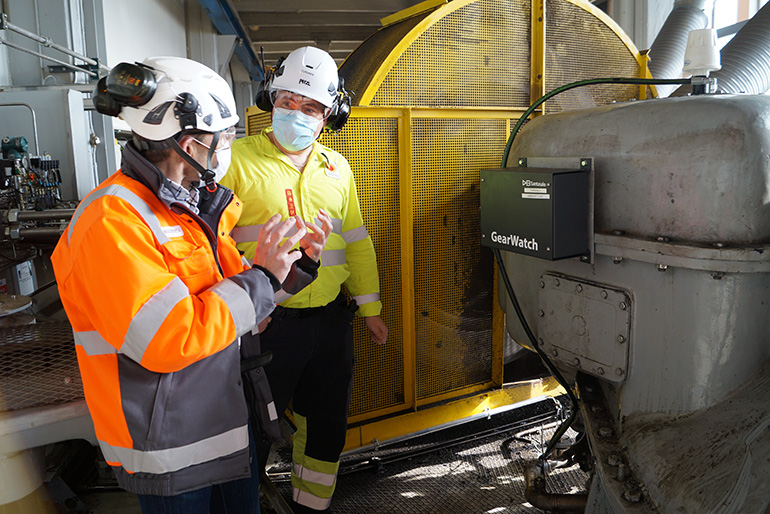 Two men talking together in front of heavy machinery..