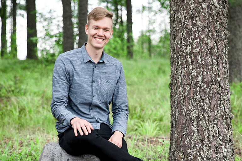 Mieshenkilö istuu kiven päällä metsässä