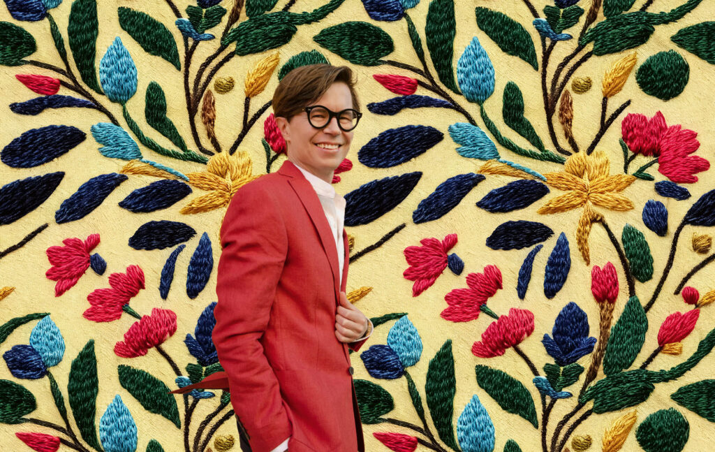 LUT-yliopiston Business Schoolin työelämäprofessori Sykkö katsoo kohti kameraa taustalla kukkakuosein koruommeltu kangas.