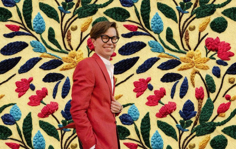 LUT-yliopiston Business Schoolin työelämäprofessori Sykkö katsoo kohti kameraa taustalla kukkakuosein koruommeltu kangas.