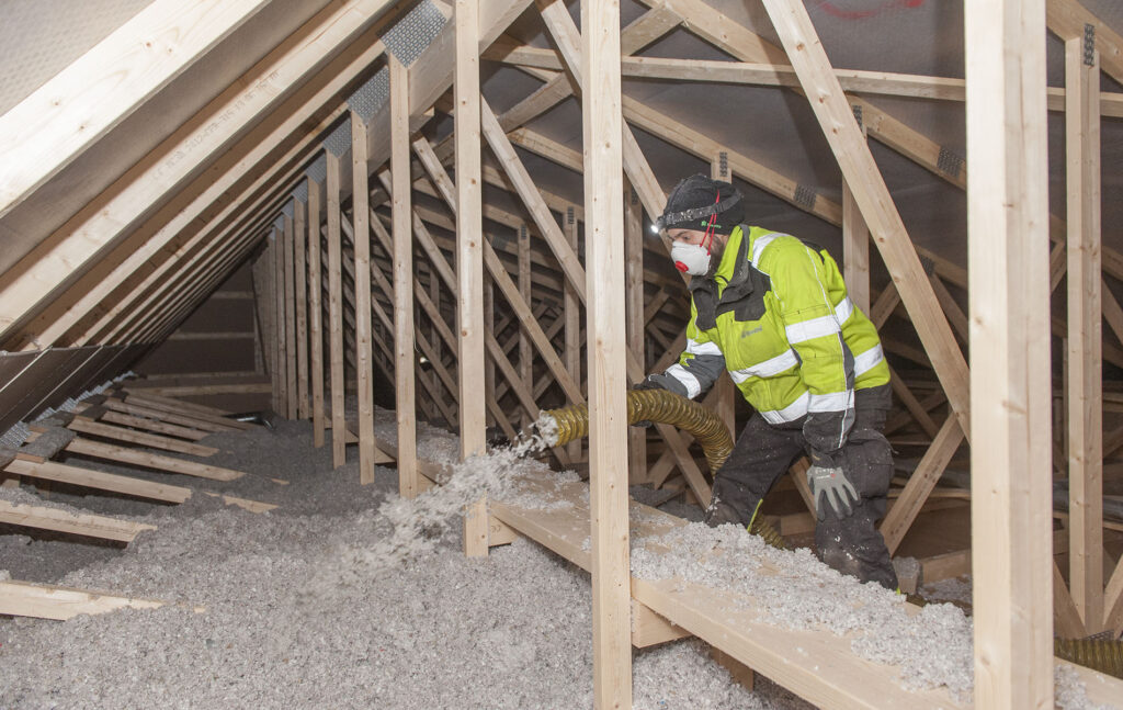 Henkilö puhaltaa rakennuksen yläpohjaan eristeeksi ekovillaa.